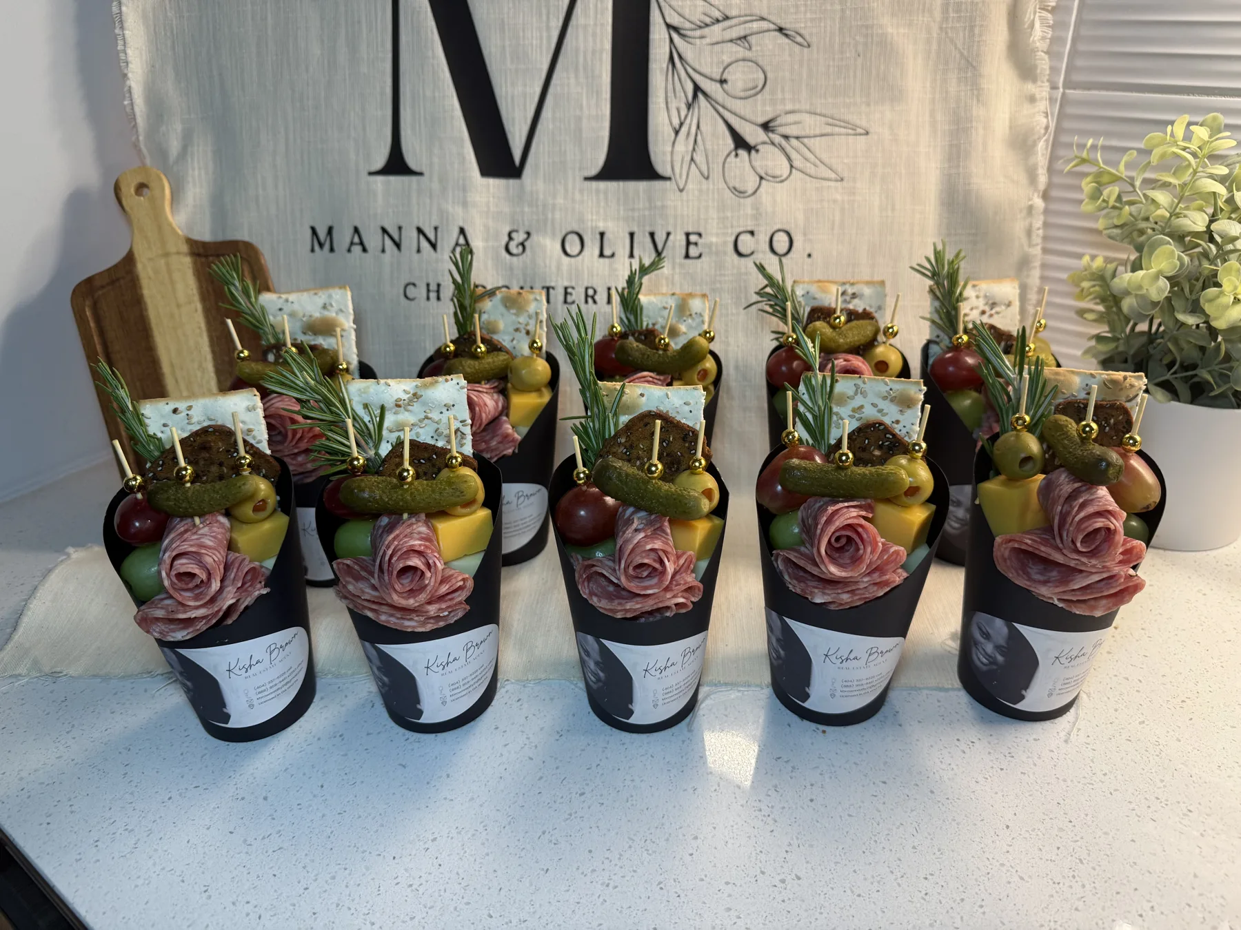 A row of branded charcuterie cups filled with salami roses, cheese, olives, crackers and fruit